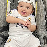 Rayan is registered to the contest to win money with this photo: baby, child, infant, smiling, happy, portrait, car_seat, sitting, sportswear, football, soccer, real_madrid, cap, white_clothing, jersey, shorts, socks, indoor, close_up, baby_carrier