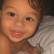 Zakar is registered to the contest to win money with this photo: baby, toddler, smiling, face, eyes, teeth, hand, curly_hair, skin, bed, pillow, white_bedclothes, child, happy, cute, indoors, portrait, person, young, holding_object