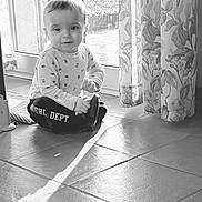 Wyllo a rejoint le concours — aidez-le/la à gagner de superbes lots ! toddler, child, indoor, floor, tile, curtains, window, glass_door, sunlight, shadow, long_sleeves, pants, patterned_clothing, sitting, baby, smiling, portrait, home, bright, young_child