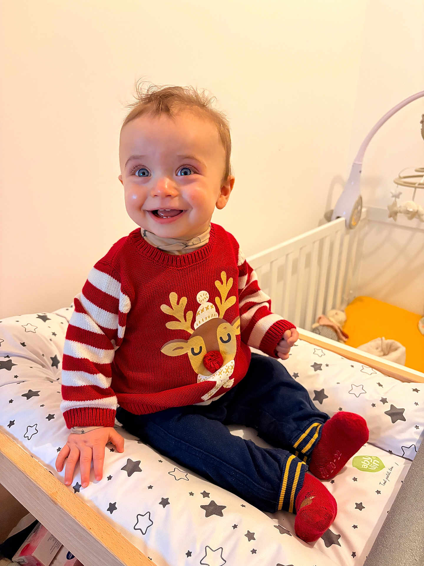Wyllo a rejoint le concours — aidez-le/la à gagner de superbes lots ! baby, child, smiling, sweater, reindeer, red, striped_sleeves, pants, socks, changing_pad, stars_pattern, nursery, crib, toys, happy, indoor, person, cute, infant, seated