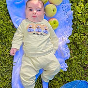 Noor is registered to the contest to win money with this photo: baby, infant, child, outdoor, grass, blanket, blue_blanket, apples, fruit, picnic, lying_down, portrait, face, wide_eyes, clothing, sweatshirt, pants, socks, garden, daylight