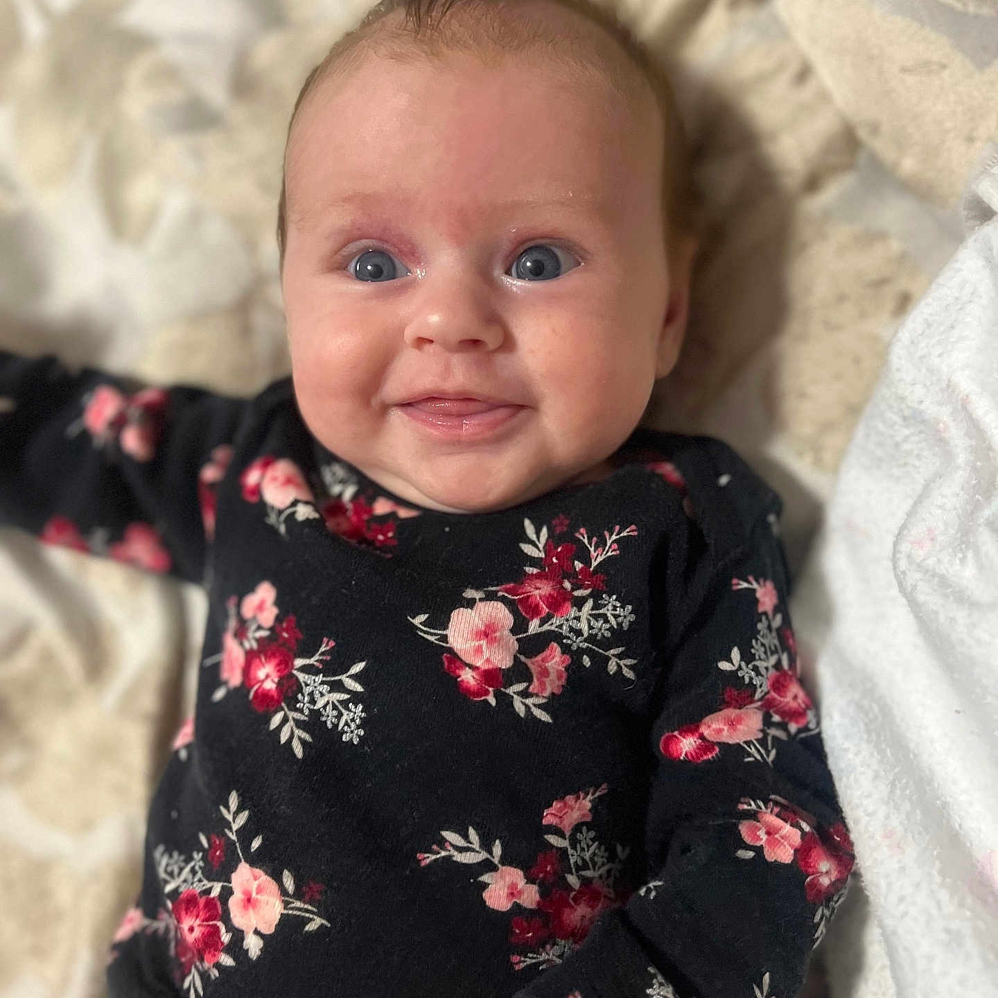 Velma-Rae is registered to the contest to win money with this photo: baby, black_outfit, blanket, blue_eyes, child, closeup, cozy, cute, face, floral_clothing, happy, indoors, infant, lying_down, person, portrait, skin, smiling, soft_texture, young_child