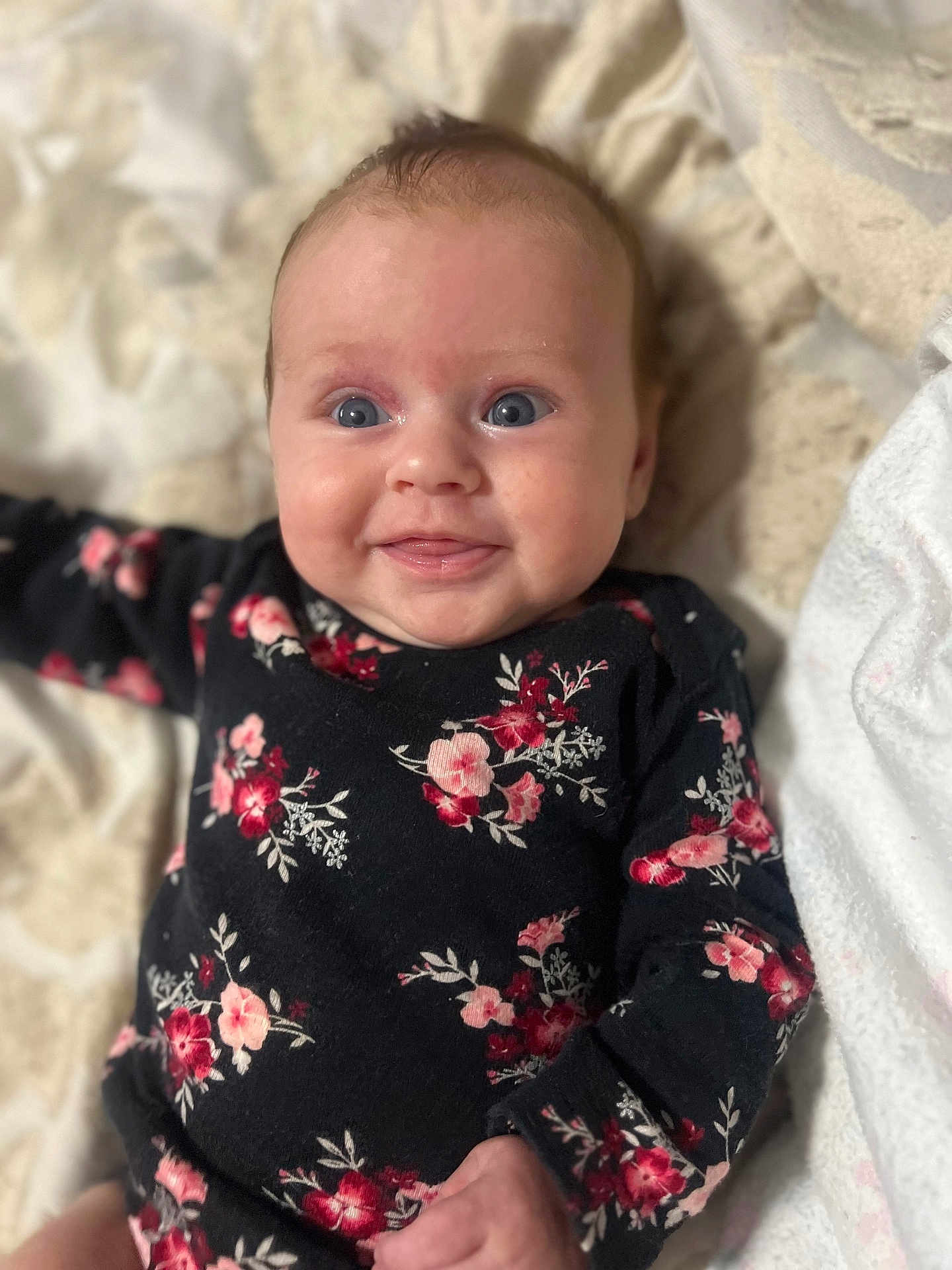 Velma-Rae is registered to the contest to win money with this photo: baby, infant, smiling, blue_eyes, floral_clothing, black_outfit, blanket, cute, portrait, child, happy, lying_down, soft_texture, indoors, young_child, closeup, skin, face, person, cozy