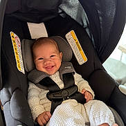 Mariano joined the competition — help win amazing prizes! baby, smiling, car_seat, infant, white_clothing, knitwear, safety_harness, happy, child, indoor, cute, person, seat, black, fabric, head_support, foot, baby_girl, portrait, childcare