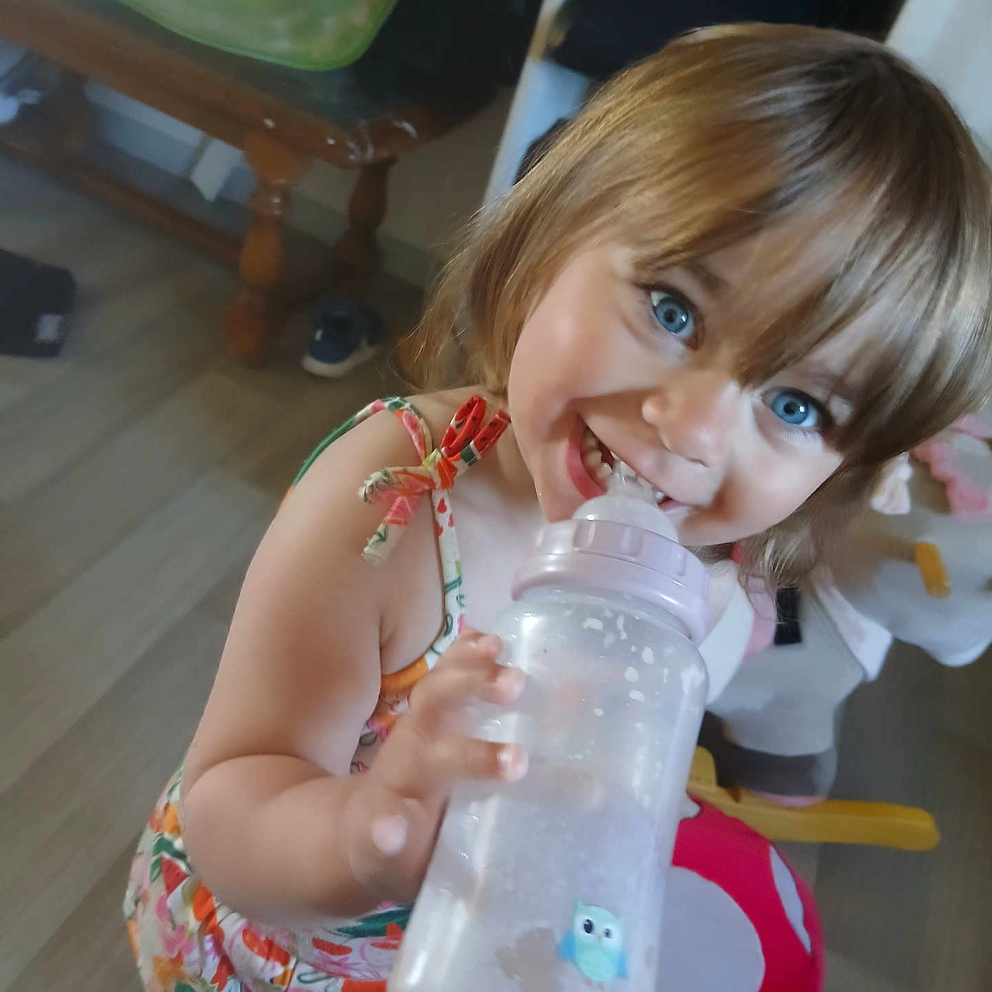 Angelina a rejoint le concours — aidez-le/la à gagner de superbes lots ! toddler, child, baby_bottle, blue_eyes, smiling, floral_outfit, indoor, floor, toy, furniture, cute, happy, person, young_child, playful, home, drinking, skin, short_hair, expression