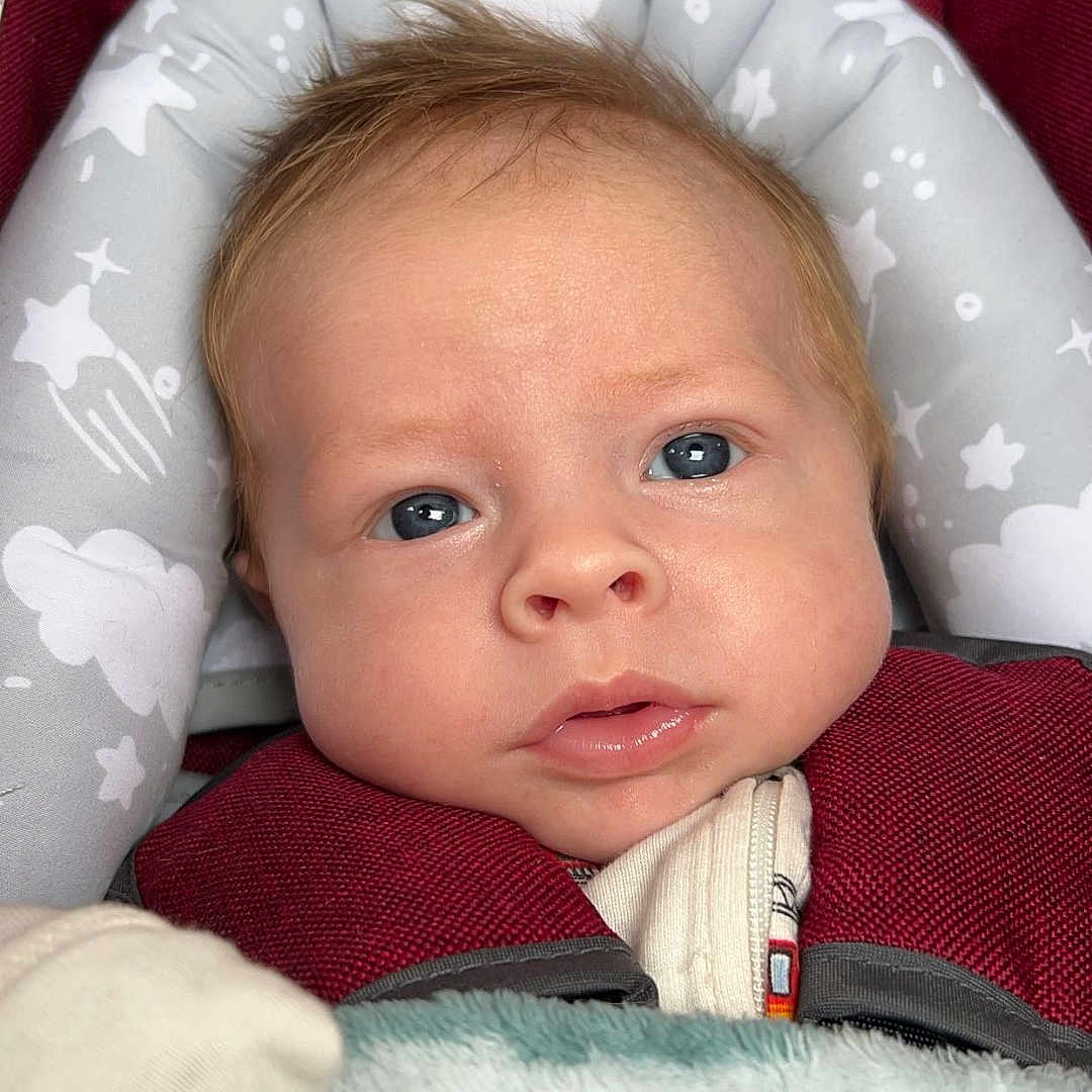 Chase is registered to the contest to win money with this photo: architecture, baby, bed, blanket, blonde, bodypart, building, car, car_interior, carseat, clothing, coat, couch, cradle, crib, cushion, face, frown, furniture, glove