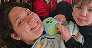 Athena Allred is registered to the contest to win money with this photo: child, adult, blanket, toy, bed, smile, family, indoor, happy, face, cuddling, person, clothing, blue_eyes, hair, pillow, red_shirt, black_shirt, playing, relaxing