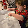 toddler, child, pajamas, christmas, holiday, ornament, wooden, marker, table, blanket, couch, decorations, red_clothing, indoor, crafting, face, person, furniture, holiday_decor, activity