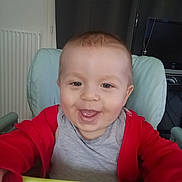 Issac participe au concours pour gagner de l'argent avec cette photo : baby, smiling, child, high_chair, red_jacket, grey_shirt, face, happy, indoor, home, furniture, radiator, television, person, cute, portrait, infant, seat, tongue_out, young