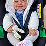 baby, car_seat, smiling, white_jacket, denim_overalls, toy, stuffed_animal, head_wrap, child, footwear, shoe, seatbelt, cute, infant, happy, portrait, indoors, closeup, pink_text, bunny_toy