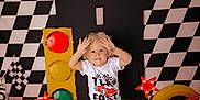 Caleb is registered to the contest to win money with this photo: checkered_flag, checkered_pattern, child, curly_hair, decor, green_light, hands_up, indoor, playful, racing_theme, red_light, red_star_light, seat, smiling, toddler, toy_car, traffic_light, white_tshirt, yellow_light, yellow_tire