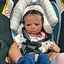 baby, infant, car_seat, straps, blue_socks, curly_hair, white_outfit, padded_cushion, safety_warning, child, seat_belt, cute, indoor, expression, face, person, newborn, small_hands, footwear, closeup