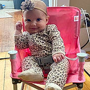 Novalee is registered to the contest to win money with this photo: baby, child, leopard_print, onesie, headband, flower, pink_chair, indoor, wooden_floor, smile, happy, cute, person, seated, footwear, belt, toy_chair, infant, home, cozy