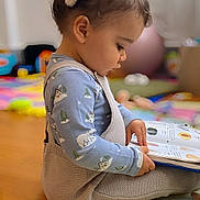 Anna a rejoint le concours — aidez-le/la à gagner de superbes lots ! toddler, child, reading, book, playmat, indoor, scrunchie, hair, clothing, long_sleeve, knit_overalls, floor, toy, colorful, window_light, side_profile, cute, young_child, playroom, focused