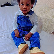 Giovanni a rejoint le concours — aidez-le/la à gagner de superbes lots ! toddler, child, denim_overalls, white_shirt, sneakers, bed, pillow, indoor, portrait, cute, curly_hair, young_child, sitting, cozy, casual_clothing, person, face, eyes, hands, home