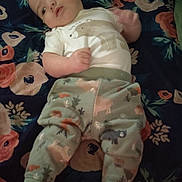 Justin is registered to the contest to win money with this photo: baby, infant, child, lying_down, floral_blanket, clothing, pants, shirt, bear_print, animal_print, foot, hand, face, head, indoors, bed, blanket, pink, blue, curious