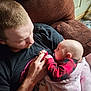 man, baby, infant, pacifier, blanket, couch, plaid, black_shirt, hand, holding, parent_child, loving_gaze, indoor, red_and_black, closeup, arm, door, floor, cozy, portrait