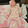 baby, infant, child, floral_clothing, pink_tights, pink_shoes, blanket, heart_pattern, couch, leather, curious, indoors, cute, small, seated, soft_lighting, fabric, footwear, person, portrait