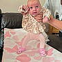 baby, infant, child, person, pink, floral_clothing, leggings, baby_shoes, hand, couch, heart_pattern, mat, indoor, wide_eyes, curious, support, adult_hand, soft_lighting, seated, portrait