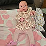 baby, infant, child, pink_shoes, floral_clothing, tights, bedspread, heart_pattern, butterfly_pattern, leather_couch, curious_expression, indoor, soft_lighting, toy_free, person, cute, small_hands, face, seated, home