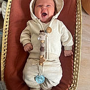 Lennon a rejoint le concours — aidez-le/la à gagner de superbes lots ! baby, infant, hoodie, pacifier, woven_basket, cushion, crocheted_toy, clothing, cozy, smiling, happy, indoors, wooden_floor, cute, newborn, lying_down, soft_fabric, child, person, relaxed