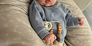 Lennon participe au concours pour gagner de l'argent avec cette photo : baby, infant, cushion, pillow, clothing, blue_sweater, beige_pants, wooden_beads, patterned_fabric, face, eyes, hand, sock, indoors, soft_lighting, cute, comfort, person, child, portrait