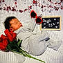 baby, newborn, sleeping, blanket, knitted_blanket, heart_sunglasses, red_sunglasses, roses, bouquet, chalkboard_sign, handwritten_text, heart_garland, hearts, props, cozy, grey_onesie, portrait, indoor, peaceful, closeup