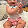 baby, child, smiling, clapping, curly_hair, bib, pink_diaper, toy_ball, indoor, floor, happy, cute, person, infant, sitting, soft_surface, home, playful, chubby_legs, closeup