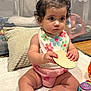 baby, child, infant, curly_hair, pink_bow, bib, toy, playpen, pillow, blanket, floor, wooden_toy, playtime, indoors, cute, sitting, clothing, young_child, expression, colorful