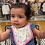 toddler, child, shopping_cart, curly_hair, pink_bows, bib, blue_outfit, store, clothing_racks, indoor, shopping, cute, baby, face, person, seatbelt, happy, eyes, hair, retail