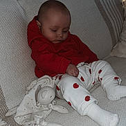 Kym a rejoint le concours — aidez-le/la à gagner de superbes lots ! baby, sleeping, red_hoodie, white_pants, hearts_pattern, plush_toy, couch, blanket, cozy, indoors, child, cute, soft_lighting, relaxation, infant, comfort, nap, clothing, homedecor, peaceful