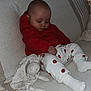 baby, sleeping, red_hoodie, white_pants, hearts_pattern, plush_toy, couch, blanket, cozy, indoors, child, cute, soft_lighting, relaxation, infant, comfort, nap, clothing, homedecor, peaceful