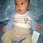 Turhan joined the competition — help win amazing prizes! baby, child, clothing, pants, shirt, tag, bed, blue, floral, sheet, person, face, hand, sitting, curious, expression, indoor, cozy, lightning_bolt, apparel