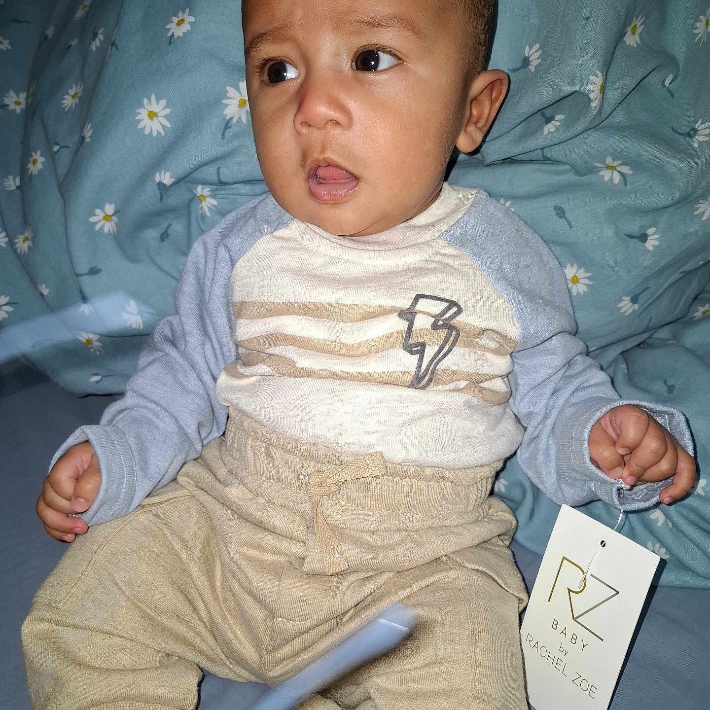 Turhan joined the competition — help win amazing prizes! apparel, baby, bed, blue, child, clothing, cozy, curious, expression, face, floral, hand, indoor, lightning_bolt, pants, person, sheet, shirt, sitting, tag