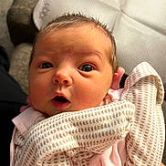 Addison is registered to the contest to win money with this photo: baby, infant, face, eyes, blanket, patterned_blanket, clothing, pink_clothing, expression, curious, surprised, newborn, human, person, indoors, soft_light, chair, hair, skin, portrait