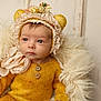Addison is registered to the contest to win money with this photo: baby, infant, yellow_outfit, knitwear, bonnet, bear_ears, flowers, fluffy_cushion, cream_color, portrait, closeup, indoors, cute, child, young, soft_texture, cozy, warm_colors, headwear, expression