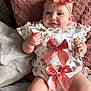 Elaya joined the competition — help win amazing prizes! baby, infant, smile, bow, headband, floral_outfit, pacifier, couch, pillow, pink, cute, child, sitting, indoors, soft_texture, legs, hands, happy, clothing, accessory