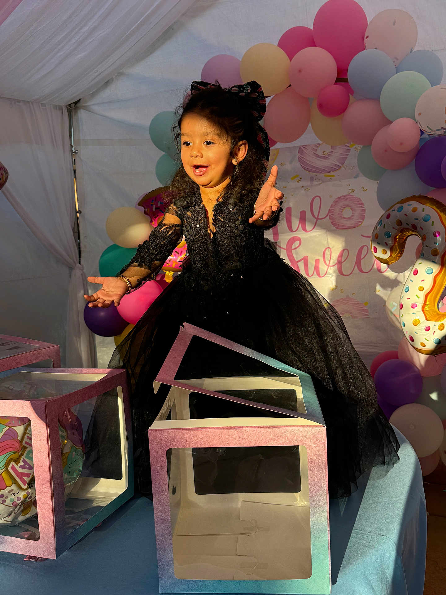 Manraj Kaur is registered to the contest to win money with this photo: child, girl, black_dress, balloons, birthday_party, number_2_balloon, gift_boxes, table, tent, smiling, happy, celebration, curly_hair, bow, colorful, party_decorations, indoors, person, young, festive