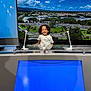 child, smile, curly_hair, microphone, news_desk, television_studio, blue_screen, cityscape, screen, technology, indoor, happy, person, broadcast, media, studio_lighting, desk, young, portrait, background