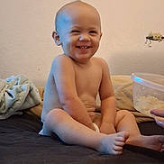 Legend is registered to the contest to win money with this photo: baby, child, infant, smiling, sitting, bed, bedroom, blanket, diaper, bare_chested, portrait, face, teeth, happy, indoor, home, container, toy, wall, photography
