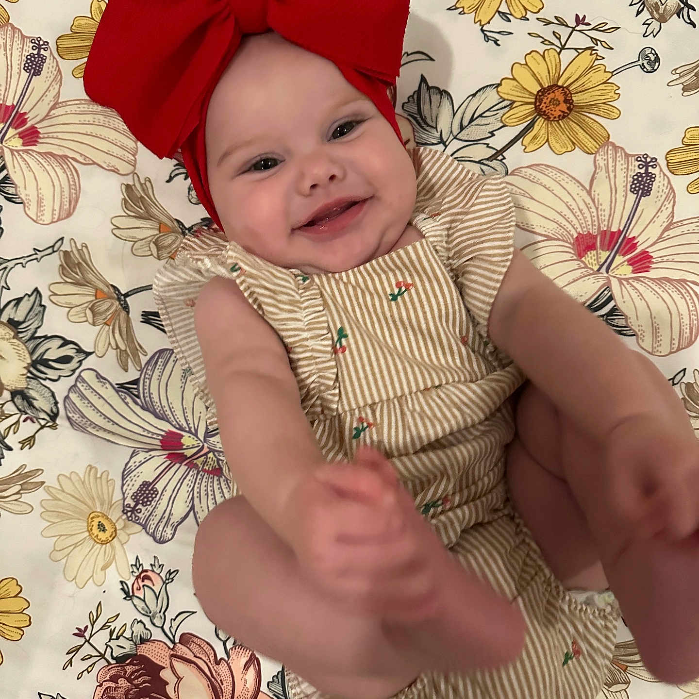 Marymae is registered to the contest to win money with this photo: baby, blanket, cheeks, child, cute, face, feet, floral_pattern, hands, happy, headband, indoors, infant, lying_down, playful, portrait, red_bow, skin, smiling, striped_clothing