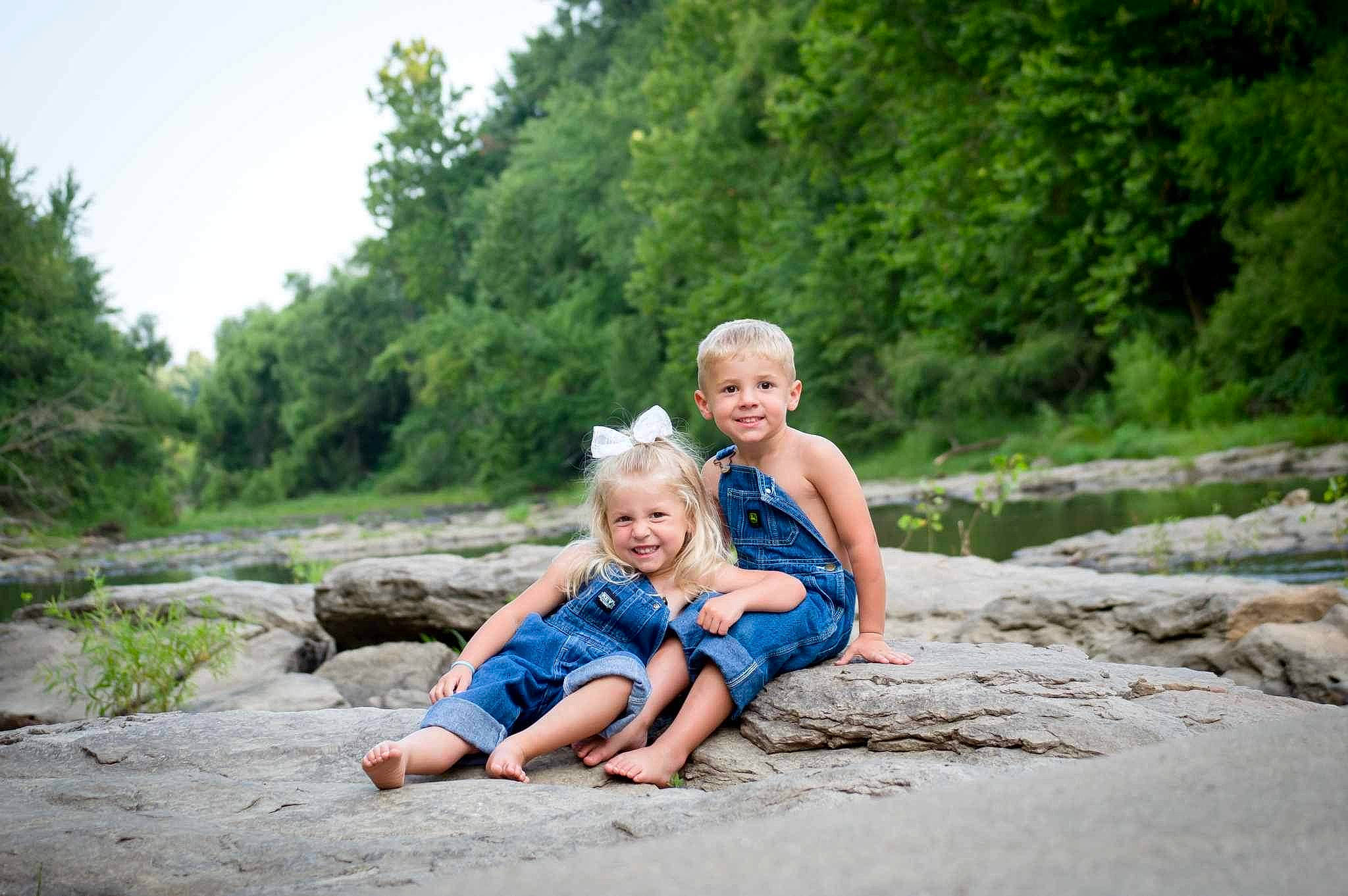 Kaislee is registered to the contest to win money with this photo: bank, forest, fun, grass, happy, joy, landscape, leisure, people_in_nature, person, plant, recreation, road, rock, sitting, sky, smile, soil, stream, toddler