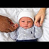 newborn, baby, infant, child, portrait, lying_down, white_bedding, bed, knit_hat, striped_clothing, onesie, long_sleeves, hands, adult_hands, family, indoor, close_up, face, awake, safe