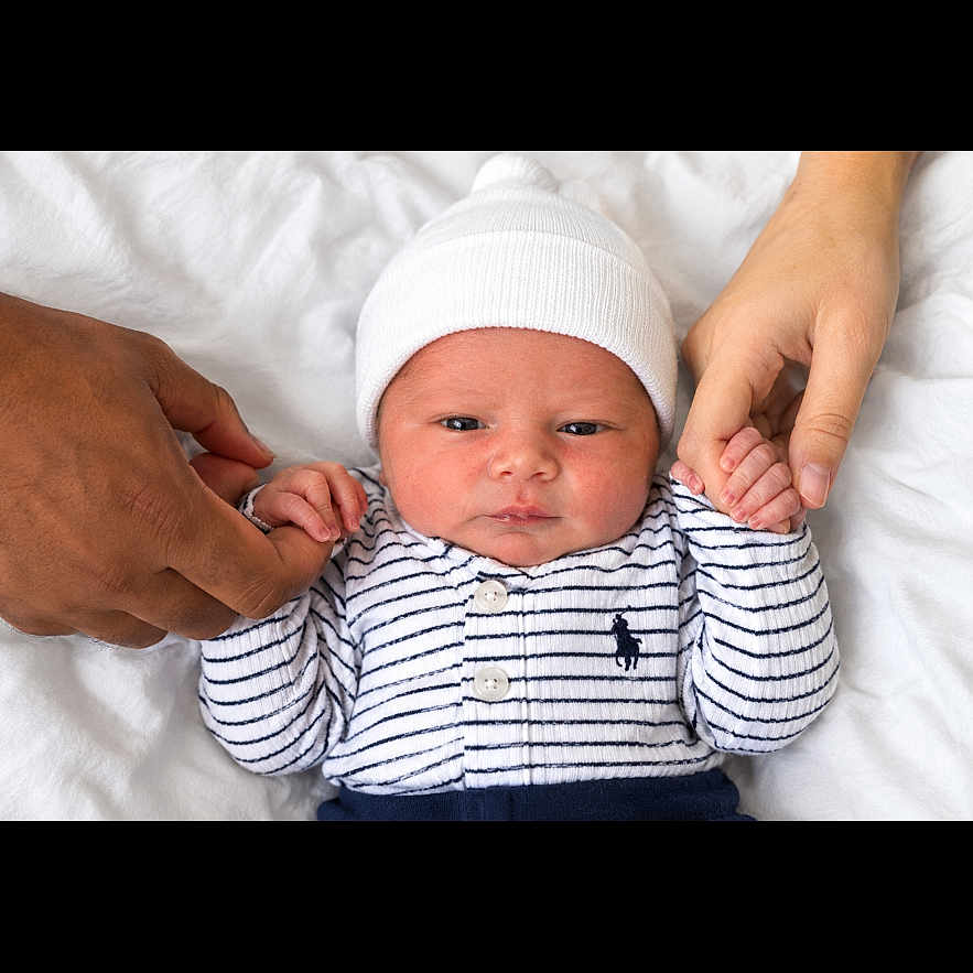 Keshawn joined the competition — help win amazing prizes! newborn, baby, infant, child, portrait, lying_down, white_bedding, bed, knit_hat, striped_clothing, onesie, long_sleeves, hands, adult_hands, family, indoor, close_up, face, awake, safe
