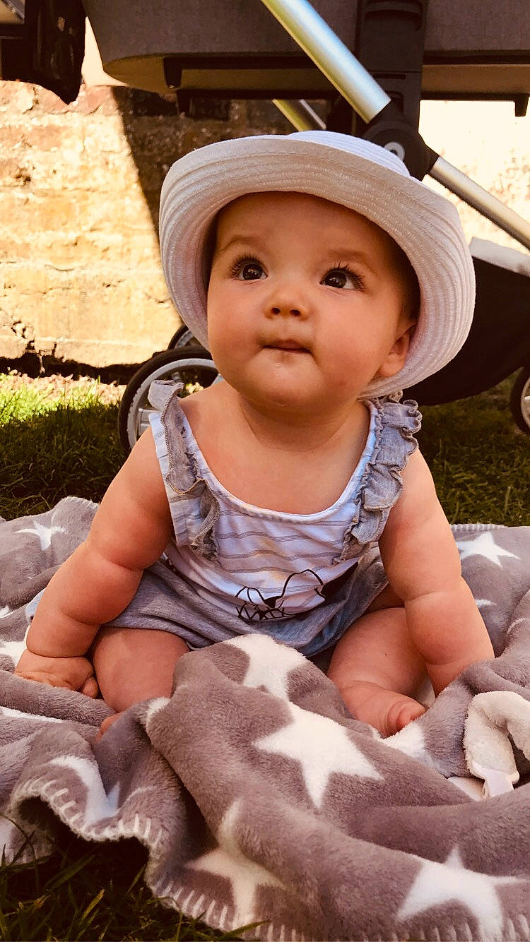 Luna a rejoint le concours — aidez-le/la à gagner de superbes lots ! baby, baby_toddler_clothing, cap, cheek, child, eye, face, fashion_accessory, fun, grass, happy, hat, headgear, headwear, mouth, person, pink, plant, sitting, skin