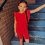braided_hair, brick_wall, casual, child, confident, expression, fashion, girl, outdoor, person, playful, portrait, posing, red_clothing, sandals, smile, sparkles, stairs, summer, young