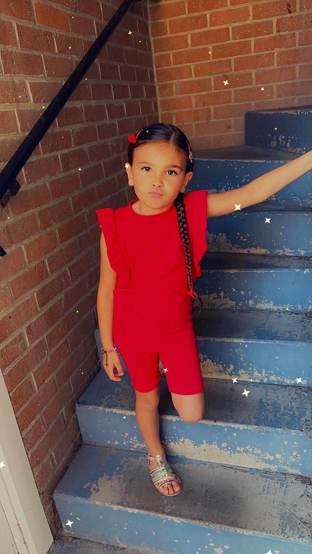 Nessïah participe au concours pour gagner de l'argent avec cette photo : braided_hair, brick_wall, casual, child, confident, expression, fashion, girl, outdoor, person, playful, portrait, posing, red_clothing, sandals, smile, sparkles, stairs, summer, young