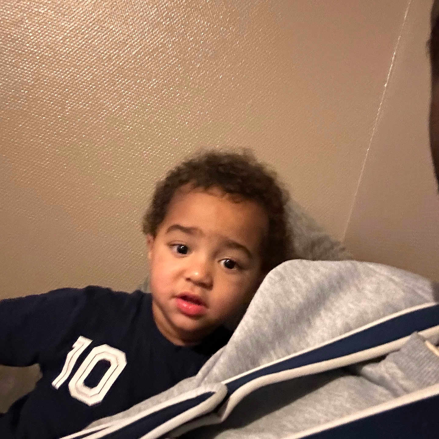 Isac a rejoint le concours — aidez-le/la à gagner de superbes lots ! blur, candid, casual, child, clothing, curious, curly_hair, expression, face, gray, indoor, jacket, leaning, navy, number_10, person, portrait, texture, wall, young