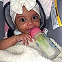 Leila is registered to the contest to win money with this photo: baby, infant, car_seat, bottle, milk, blanket, headband, bow, cute, face, hand, clothing, child, indoors, seat, smiling, person, closeup, baby_bottle, warm