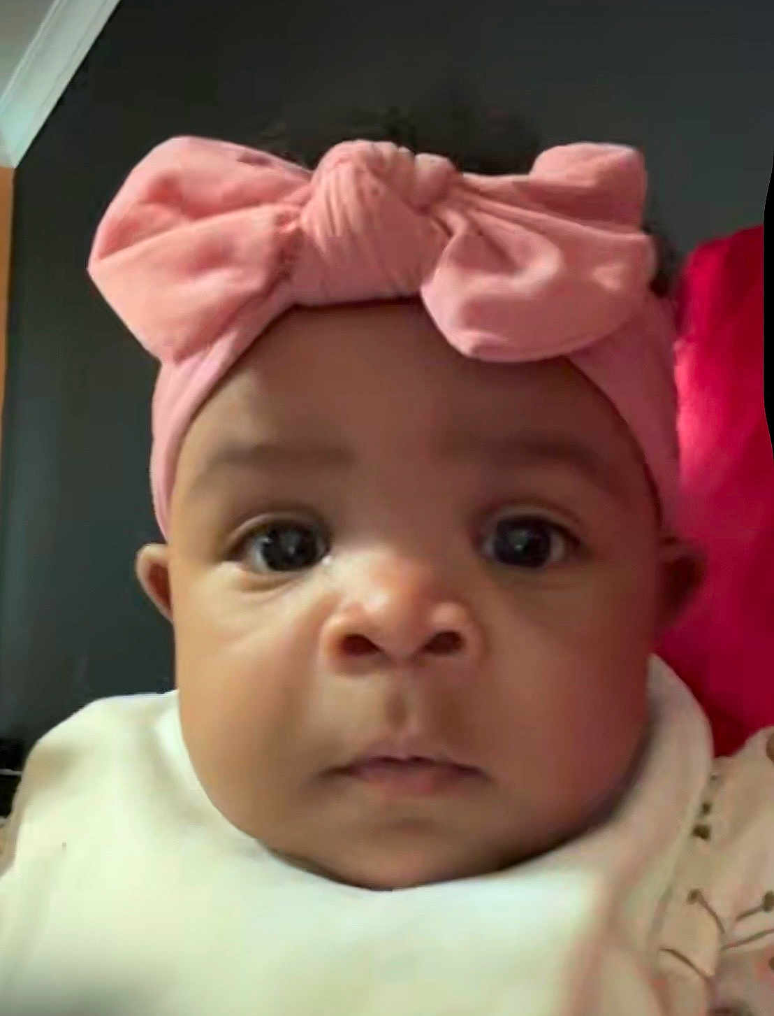 Blessynn is registered to the contest to win money with this photo: baby, infant, newborn, face, eyes, cheeks, headband, bow, pink_bow, bib, close_up, portrait, indoor, pillow, dark_background, expression, curious, adorable, skin, clothing